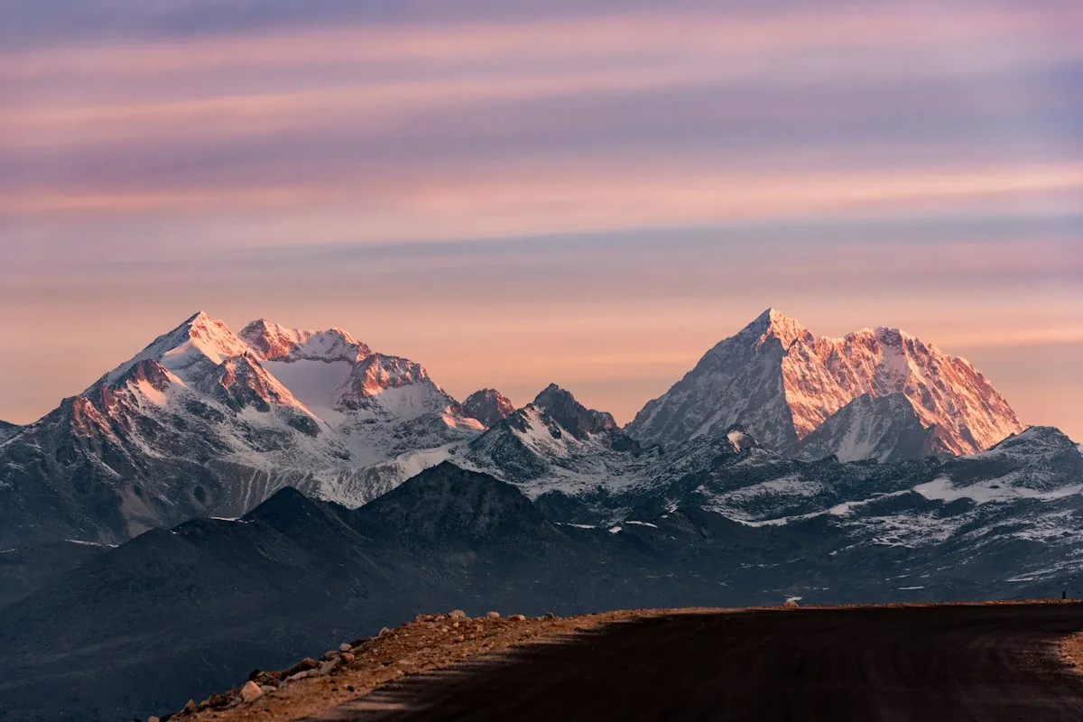 Snow peaks lit pink by the setting sun above a dark ridge
