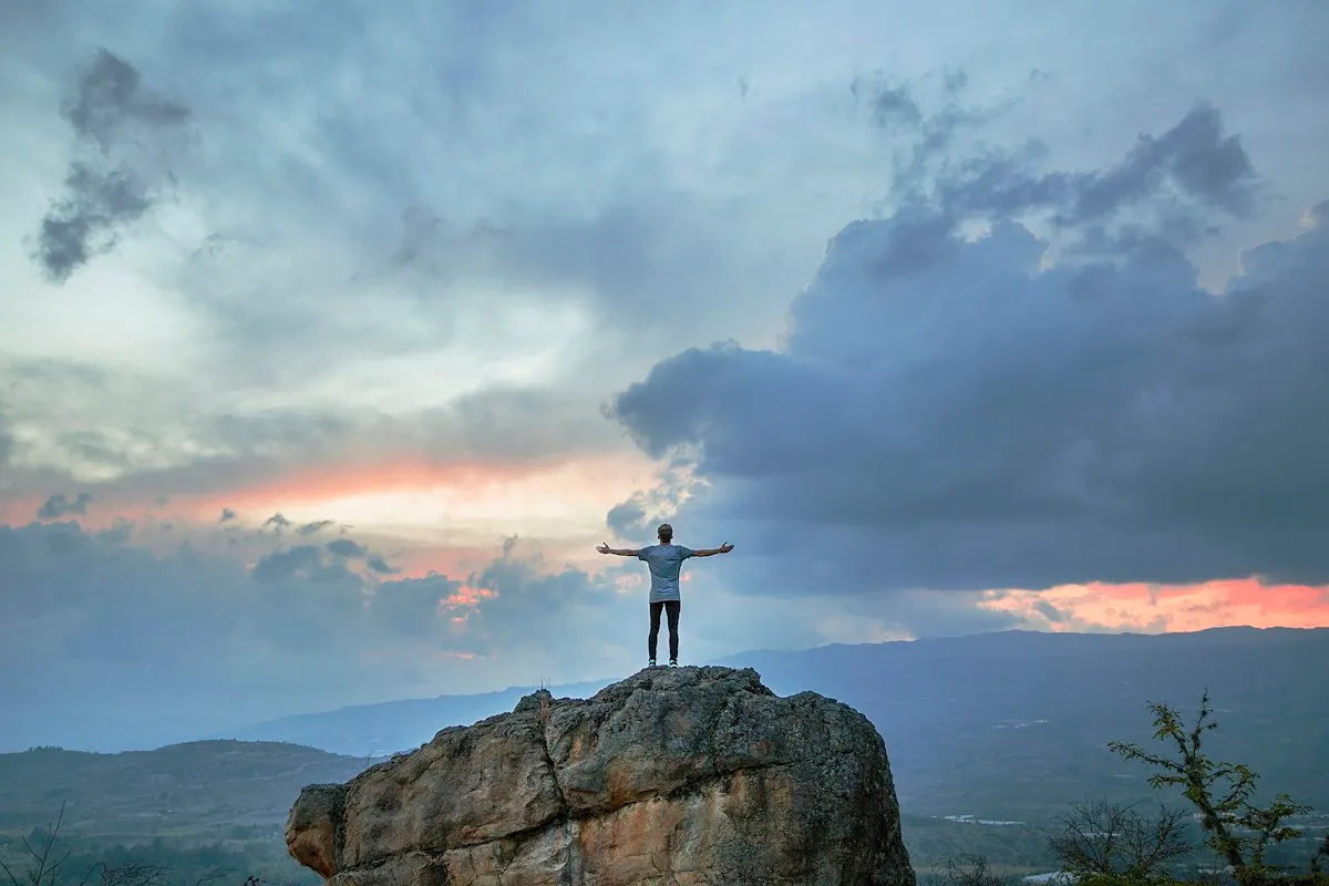 Hiker with arms raised on a rocky summit at sunset